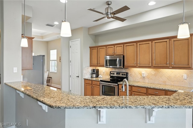 178 Shadroe Cove Cir Unit 903, Cape Coral, FL 33991 - kitchen with appliances with stainless steel finishes, brown cabinetry, backsplash, light stone counters, and a breakfast bar