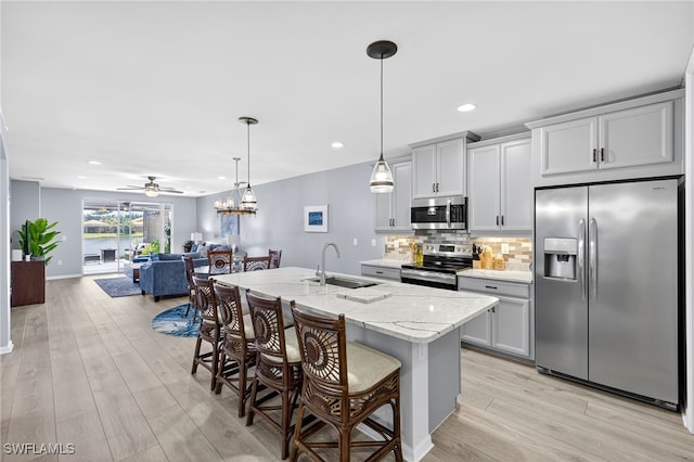 14803 Edgewater Cir, Naples, FL 34114 - kitchen with appliances with stainless steel finishes, a breakfast bar area, light wood-type flooring, an island with sink, and decorative backsplash