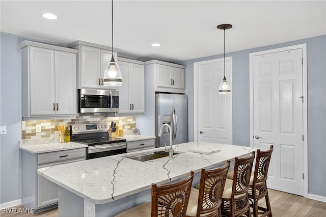 14803 Edgewater Cir, Naples, FL 34114 - kitchen featuring appliances with stainless steel finishes, a kitchen bar, backsplash, light wood-style floors, and light stone countertops