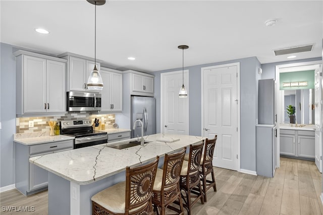 14803 Edgewater Cir, Naples, FL 34114 - kitchen featuring appliances with stainless steel finishes, light wood finished floors, tasteful backsplash, a breakfast bar area, and light stone countertops