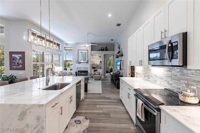4372 Bittern Ct, Naples, FL 34119 - kitchen with stainless steel appliances, ceiling fan, an island with sink, decorative backsplash, and wood finished floors