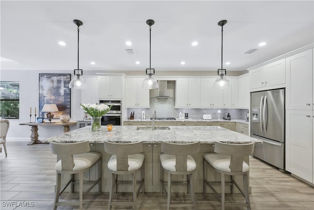 10082 Palazzo Dr, Naples, FL 34119 - kitchen with appliances with stainless steel finishes, wall chimney range hood, tasteful backsplash, an island with sink, and white cabinets