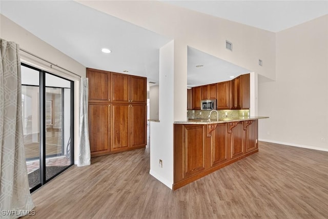 8060 Glenfinnan Cir, Fort Myers, FL 33912 - kitchen with stainless steel microwave, light wood-style flooring, brown cabinetry, a breakfast bar area, and backsplash