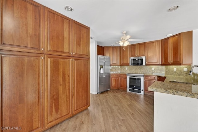 8060 Glenfinnan Cir, Fort Myers, FL 33912 - kitchen with stainless steel appliances, a ceiling fan, light wood-style floors, backsplash, and brown cabinets