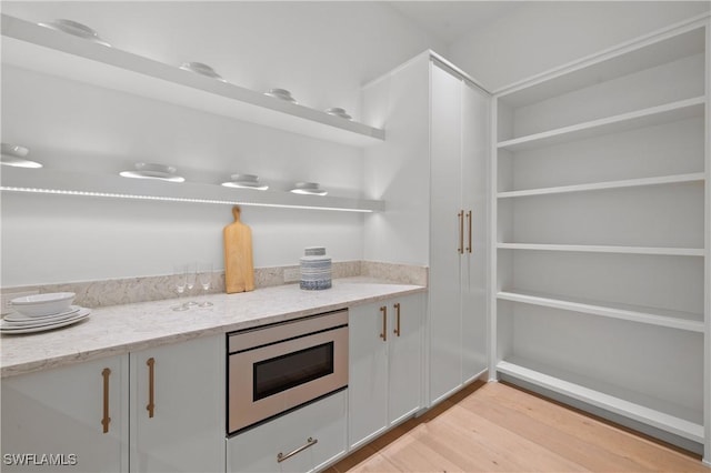 850 10th St N, Naples, FL 34102 - kitchen featuring stainless steel microwave, open shelves, light wood-type flooring, light stone counters, and white cabinets