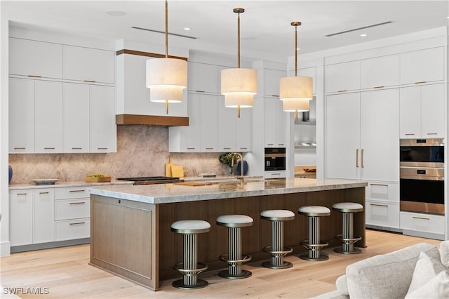 850 10th St N, Naples, FL 34102 - kitchen featuring a kitchen bar, light wood-style flooring, decorative backsplash, an island with sink, and recessed lighting
