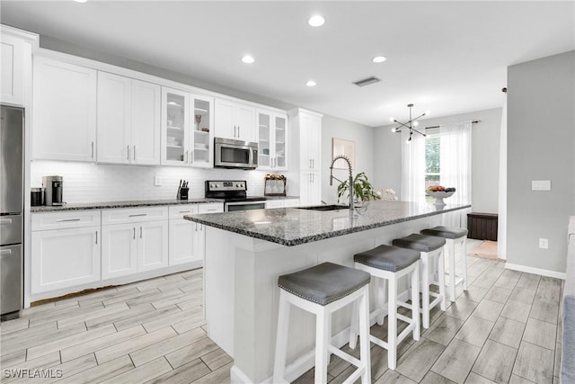 8094 Silver Birch Way, Lehigh Acres, FL 33971 - kitchen with appliances with stainless steel finishes, white cabinetry, wood finish floors, dark stone countertops, and a kitchen breakfast bar