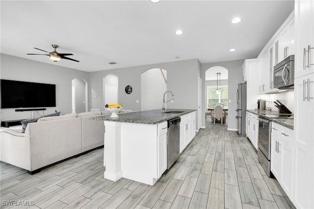 8094 Silver Birch Way, Lehigh Acres, FL 33971 - kitchen with stainless steel appliances, white cabinetry, dark stone counters, arched walkways, and recessed lighting
