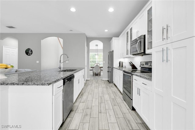 8094 Silver Birch Way, Lehigh Acres, FL 33971 - kitchen with stainless steel appliances, arched walkways, glass insert cabinets, white cabinets, and dark stone counters