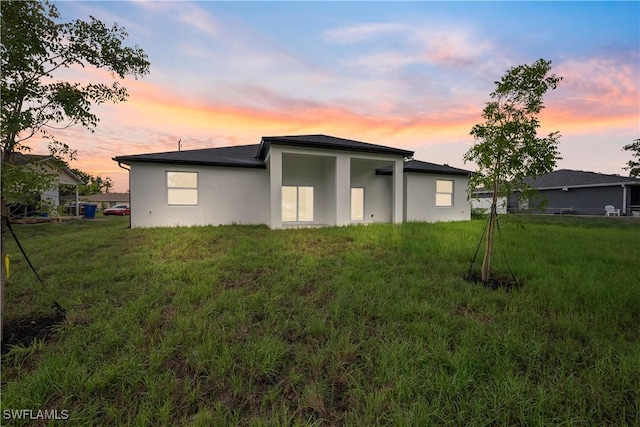 2429/2431 Lola Ave S, Lehigh Acres, FL 33973 - back of property at dusk featuring stucco siding and a yard