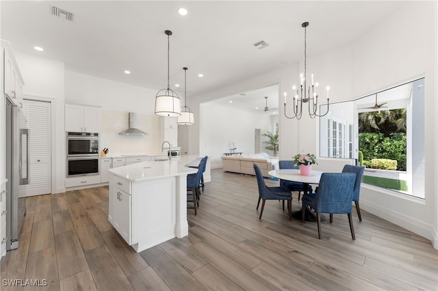 2274 Hawksridge Dr, Naples, FL 34105 - kitchen featuring wall chimney range hood, multiple ovens, light countertops, light wood-style floors, and open floor plan
