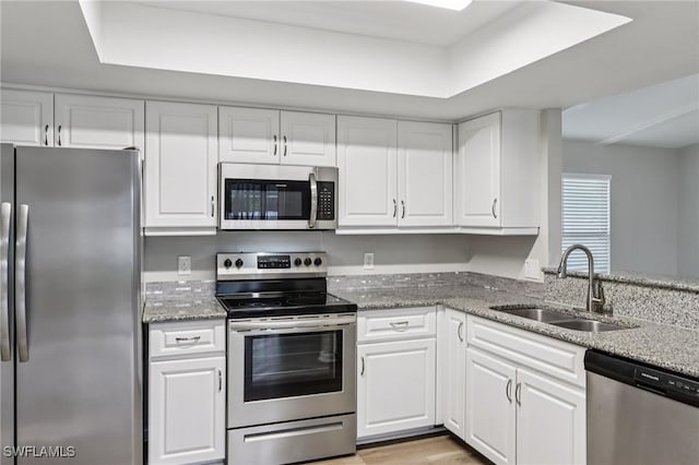 740 SW 5th St, Cape Coral, FL 33991 - kitchen featuring appliances with stainless steel finishes, white cabinetry, light stone counters, light wood-style floors, and a tray ceiling