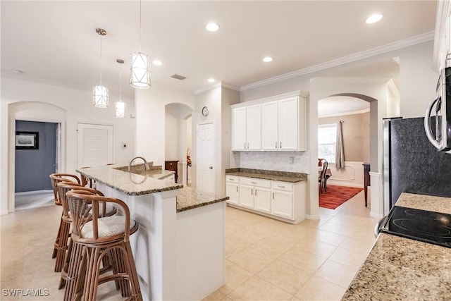 3260 Magnolia Landing Ln, North Fort Myers, FL 33917 - kitchen featuring arched walkways, a kitchen bar, light stone counters, white cabinetry, and ornamental molding