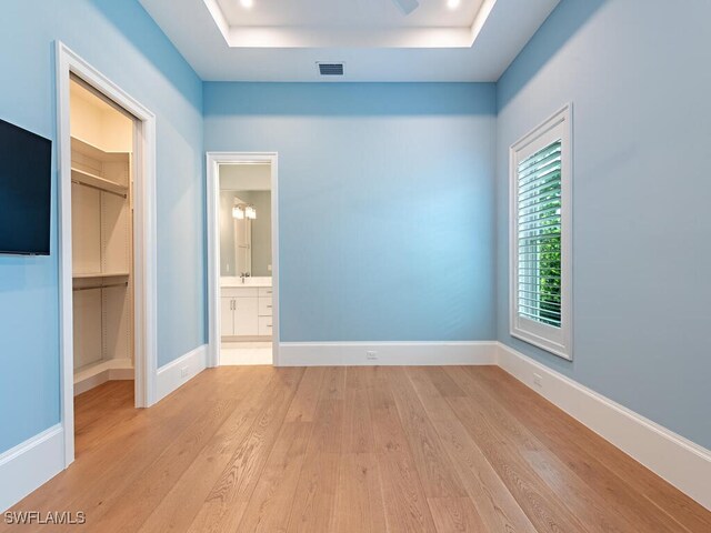 130 Burning Tree Dr, Naples, FL 34105 - unfurnished bedroom with wood finished floors, a spacious closet, a tray ceiling, a closet, and ensuite bathroom