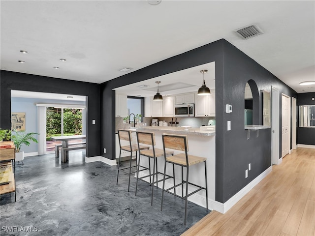11810 Imperial Pines Way, Bonita Springs, FL 34135 - kitchen with stainless steel microwave, white cabinets, a breakfast bar area, a peninsula, and pendant lighting