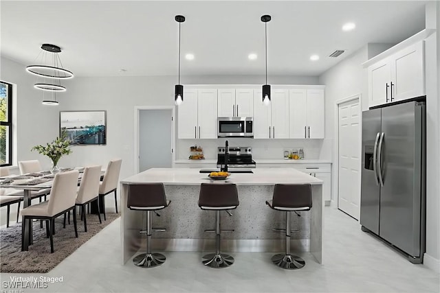 1002 E 17th St, Lehigh Acres, FL 33972 - kitchen with stainless steel appliances, white cabinets, light countertops, a center island with sink, and pendant lighting