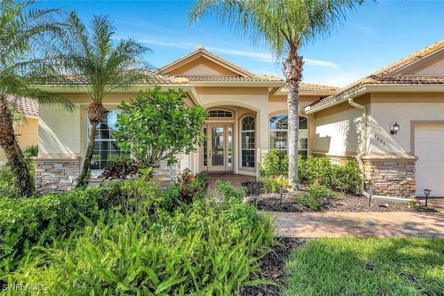 9693 Cobalt Cove Cir, Naples, FL 34120 - doorway to property featuring stucco siding, stone siding, and a garage