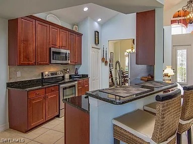 27329 Jolly Roger Ln, Bonita Springs, FL 34135 - kitchen with stainless steel appliances, a chandelier, dark stone countertops, a kitchen bar, and light tile patterned floors