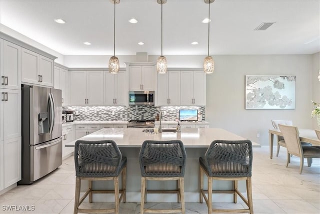 28646 Lobos Cir, Bonita Springs, FL 34135 - kitchen with appliances with stainless steel finishes, light countertops, decorative backsplash, a breakfast bar area, and an island with sink