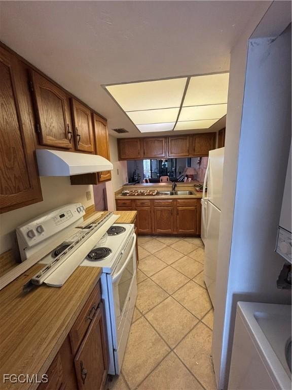 4265 Bay Beach Ln Unit 524, Fort Myers Beach, FL 33931 - kitchen featuring white appliances, light tile patterned floors, under cabinet range hood, brown cabinetry, and light countertops