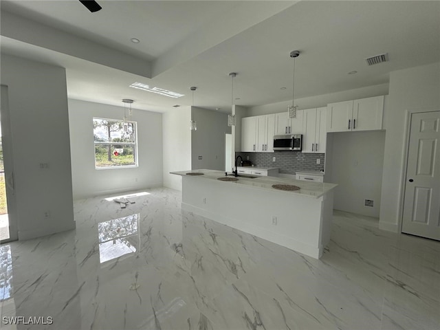 1402 Henry Ave, Lehigh Acres, FL 33972 - kitchen with stainless steel microwave, white cabinetry, tasteful backsplash, a center island with sink, and pendant lighting