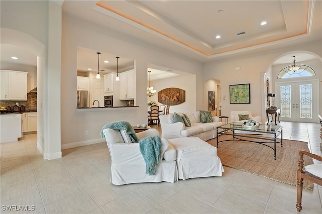 23484 Sanabria Loop, Bonita Springs, FL 34135 - living room featuring arched walkways, a raised ceiling, french doors, light tile patterned floors, and a chandelier