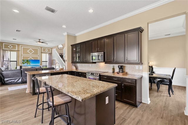 5158 Roma St, Ave Maria, FL 34142 - kitchen featuring appliances with stainless steel finishes, dark brown cabinets, a kitchen breakfast bar, a ceiling fan, and light stone countertops