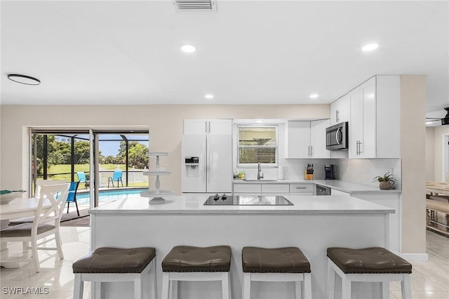 3823 Palm Tree Blvd, Cape Coral, FL 33904 - kitchen featuring white fridge with ice dispenser, stainless steel microwave, black electric cooktop, a breakfast bar area, and light countertops