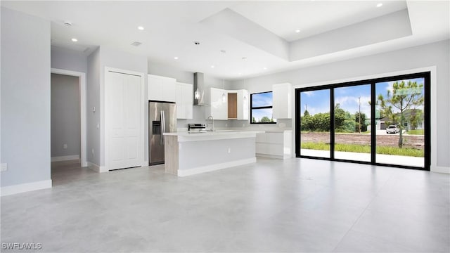 766 Naples Ave S, Lehigh Acres, FL 33974 - kitchen with stainless steel fridge, wall chimney exhaust hood, light countertops, a kitchen island with sink, and white cabinetry