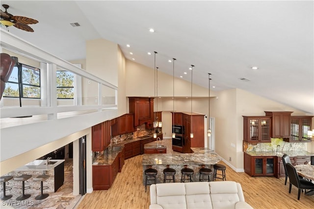 1701 Casey Key Dr, Punta Gorda, FL 33950 - kitchen featuring light wood-style flooring, high vaulted ceiling, tasteful backsplash, light stone countertops, and a kitchen breakfast bar