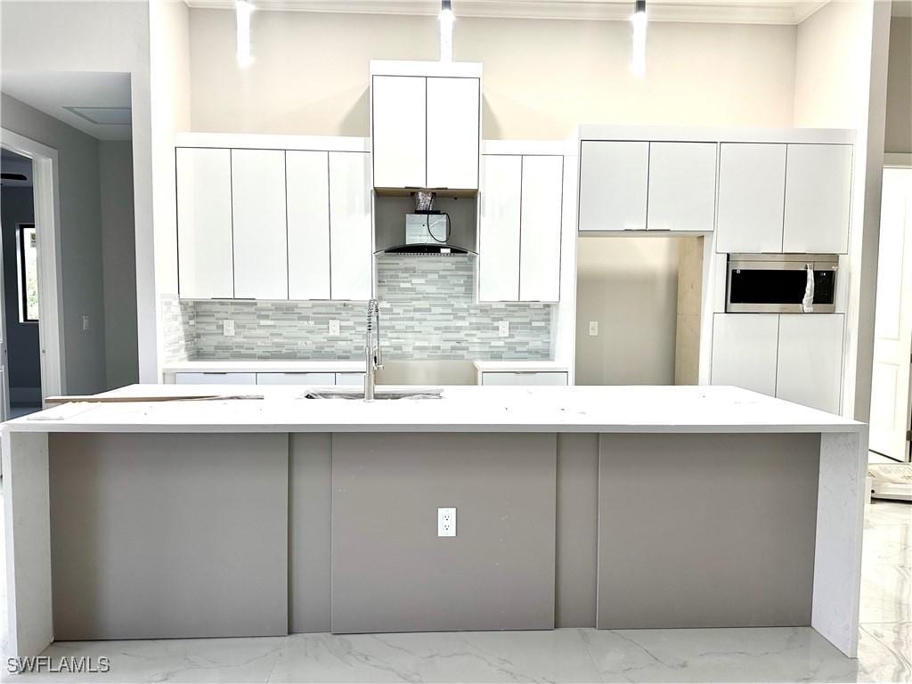 3201 2nd St SW, Lehigh Acres, FL 33976 - kitchen featuring stainless steel microwave, white cabinets, tasteful backsplash, and a kitchen island with sink