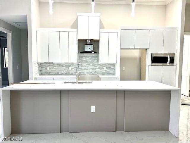 3201 2nd St SW, Lehigh Acres, FL 33976 - kitchen featuring stainless steel microwave, white cabinets, tasteful backsplash, and a kitchen island with sink