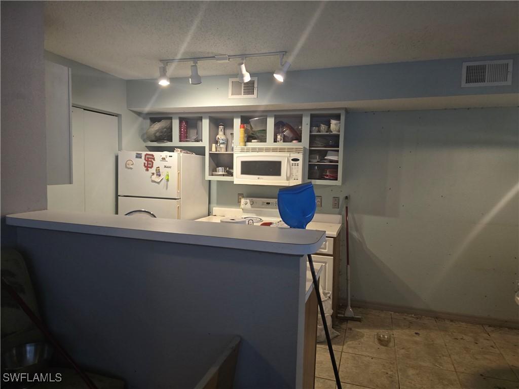 12551 Equestrian Cir Unit 704, Fort Myers, FL 33907 - kitchen with white appliances, open shelves, rail lighting, a peninsula, and light countertops