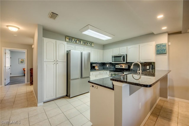 841 SW 47th Ter Unit 206, Cape Coral, FL 33914 - kitchen featuring appliances with stainless steel finishes, a peninsula, dark stone countertops, light tile patterned floors, and white cabinets