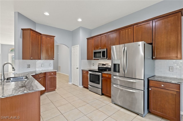 8169 Silver Birch Way, Lehigh Acres, FL 33971 - kitchen featuring appliances with stainless steel finishes, arched walkways, backsplash, light stone countertops, and a peninsula