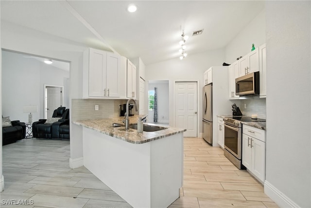 2711 4th St NW, Naples, FL 34120 - kitchen with stainless steel appliances, white cabinetry, a peninsula, decorative backsplash, and wood tiled floors