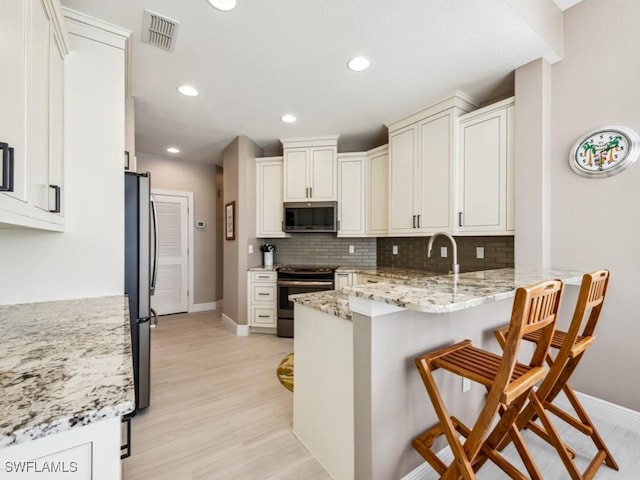 26690 Egrets Landing Dr Unit 101, Bonita Springs, FL 34134 - kitchen featuring stainless steel appliances, a peninsula, tasteful backsplash, white cabinetry, and a kitchen breakfast bar