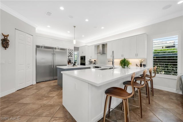 3910 Glacier Ct, Naples, FL 34119 - kitchen featuring built in appliances, ornamental molding, a peninsula, backsplash, and wall chimney exhaust hood