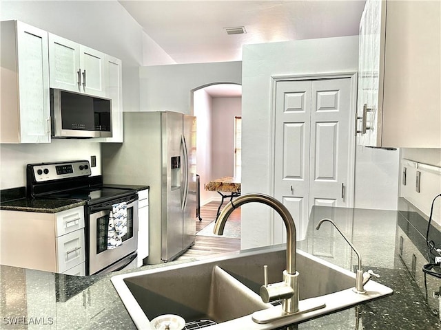 2675 70th Ave NE, Naples, FL 34120 - kitchen with stainless steel appliances, arched walkways, white cabinetry, and dark stone counters
