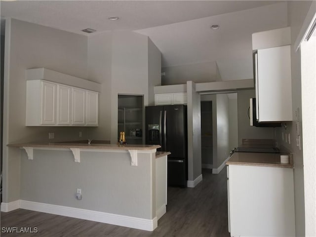 23447 Olde Meadowbrook Cir, Estero, FL 34134 - kitchen featuring black fridge with ice dispenser, a peninsula, a kitchen bar, dark wood finished floors, and white cabinetry