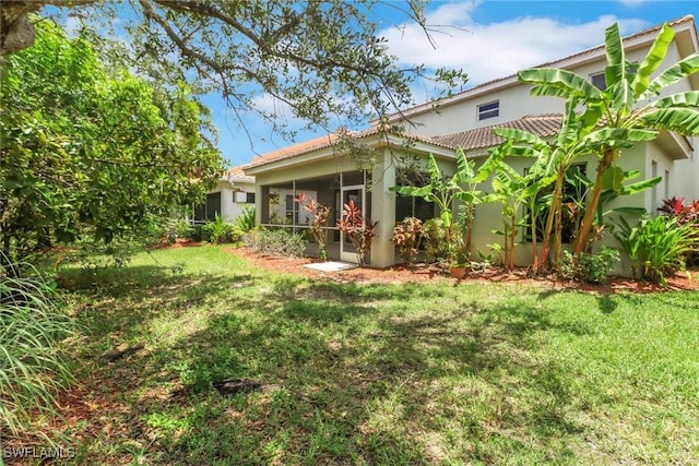 8677 Pegasus Dr, Lehigh Acres, FL 33971 - rear view of property featuring a lawn, stucco siding, a sunroom, and a tiled roof