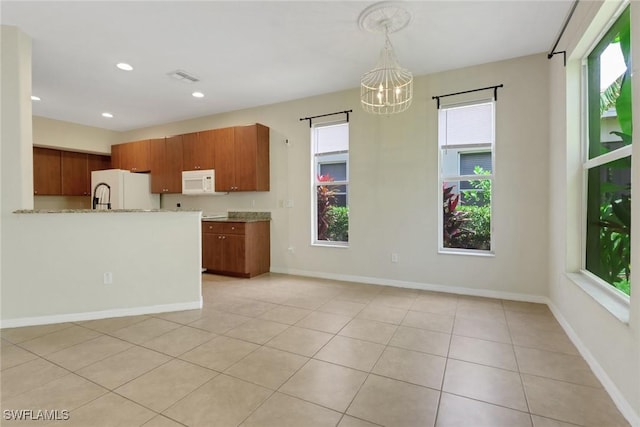 8677 Pegasus Dr, Lehigh Acres, FL 33971 - kitchen with white appliances, a chandelier, brown cabinetry, light tile patterned floors, and recessed lighting