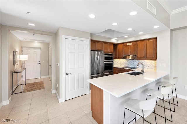 2738 Tiburon Blvd E Unit B406, Naples, FL 34109 - kitchen featuring under cabinet range hood, a peninsula, brown cabinetry, stainless steel appliances, and a breakfast bar area