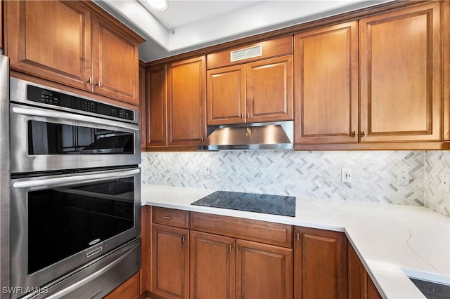 2738 Tiburon Blvd E Unit B406, Naples, FL 34109 - kitchen with stainless steel double oven, black electric stovetop, under cabinet range hood, a warming drawer, and brown cabinetry
