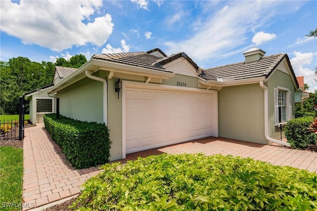 15139 Ligustrum Ln, Alva, FL 33920 - view of property exterior featuring stucco siding, a tiled roof, an attached garage, a chimney, and driveway