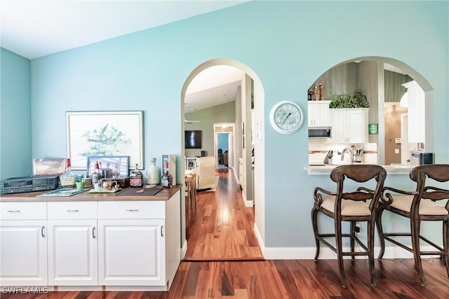 15139 Ligustrum Ln, Alva, FL 33920 - kitchen with stainless steel microwave, wood finished floors, white cabinetry, vaulted ceiling, and a kitchen breakfast bar