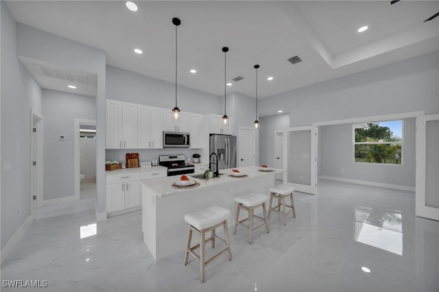 3706 16th St W, Lehigh Acres, FL 33971 - kitchen featuring stainless steel appliances, light marble finish flooring, white cabinets, a breakfast bar area, and a kitchen island with sink