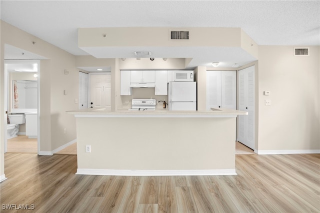 8851 Colonnades Ct W Unit 128, Bonita Springs, FL 34135 - kitchen featuring white appliances, light wood-type flooring, under cabinet range hood, white cabinets, and light countertops