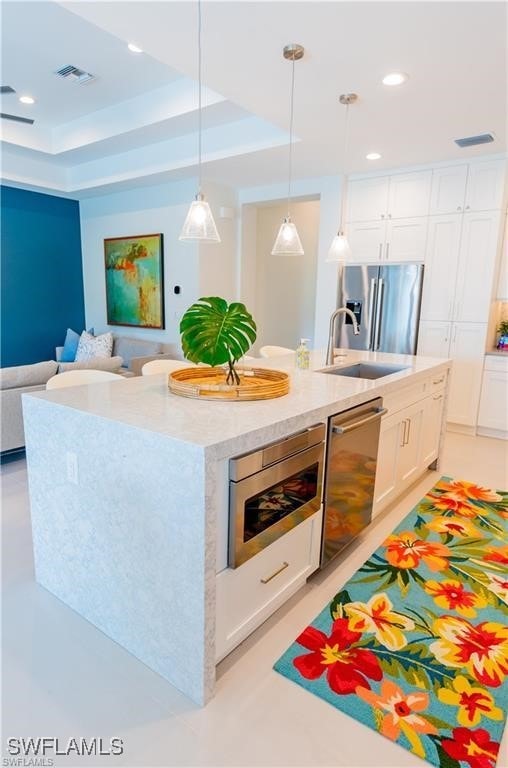 756 108th Ave N, Naples, FL 34108 - kitchen featuring appliances with stainless steel finishes, white cabinetry, a center island with sink, open floor plan, and decorative light fixtures