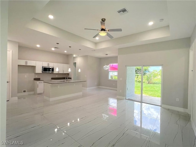 4208 28th St SW, Lehigh Acres, FL 33976 - kitchen featuring stainless steel microwave, a tray ceiling, light marble finish flooring, open floor plan, and white cabinetry